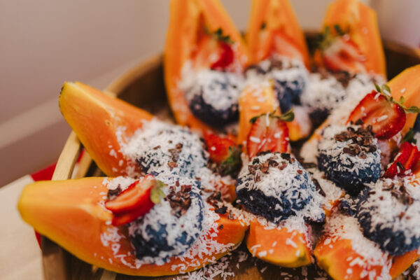 A wooden bowl filled with papaya slices topped with blueberries, shredded coconut, and sliced strawberries. This colorful and inviting presentation is the kind of artistry you can expect from Lotus Chefs Maui private chef services for plant-based retreat catering.