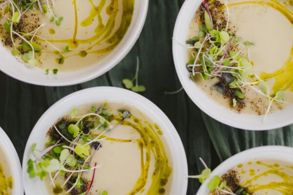 White bowls filled with creamy soup, drizzled with olive oil and topped with microgreens and a sprinkle of ground black pepper, arranged on a dark green cloth—a masterpiece reflective of the exquisite touch only a Maui personal chef can provide.