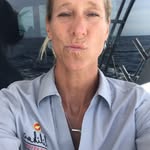 A person with blond hair, wearing a light blue collared shirt, takes a selfie on a boat with the ocean and rails visible in the background, capturing a moment reminiscent of Chef Maja Liotta’s seaside adventures.