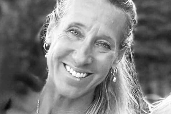 Smiling woman with long, light hair pulled to one side, wearing earrings and a necklace, photographed outdoors with a blurred background—Chef Maja Liotta exudes warmth and elegance in this candid moment.